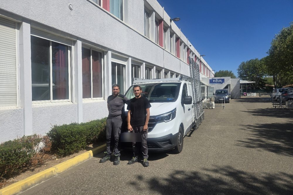Deux membres de l'équipe JBE Automatisme devant le camion d'intervention, matériel chargé sur la galerie, sur le parking d'un bâtiment