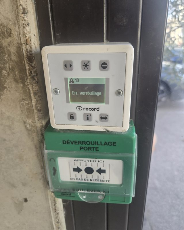 Panneau de commande d'une porte automatique affichant un code de défaut de verrouillage, boîtier vert de déverrouillage d'urgence en dessous