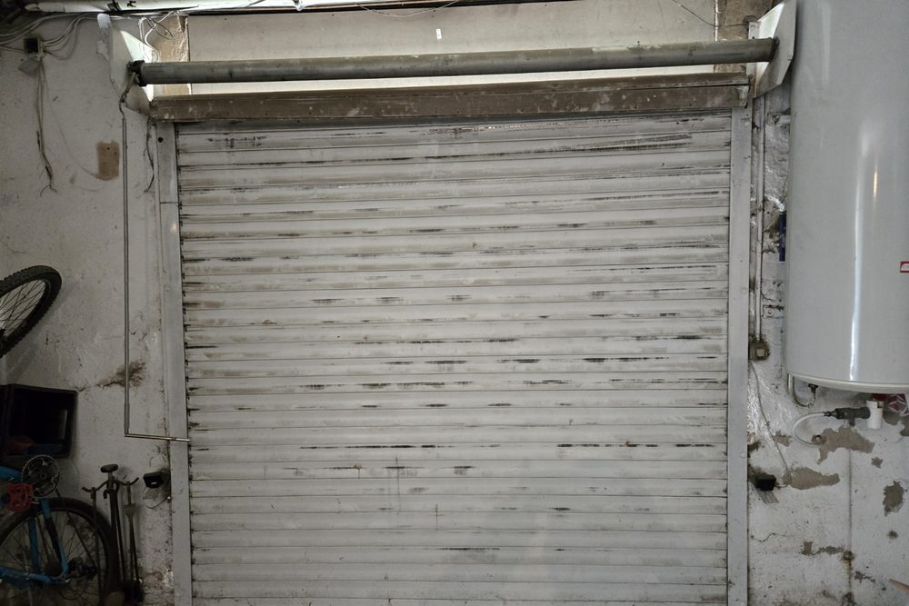 Rideau métallique blanc fermé dans un garage, vu de l'intérieur, montants et axe visibles